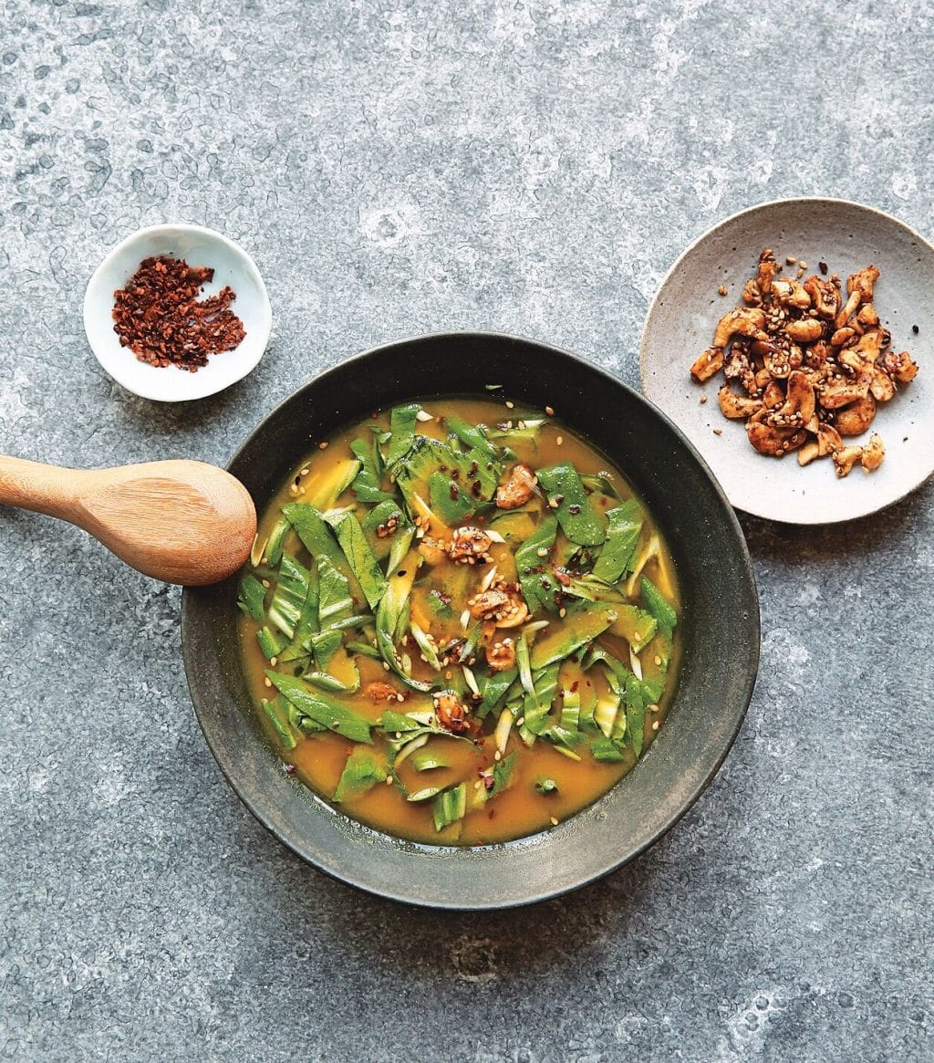 miso broth in a black dish with a wood spoon on the rim and two dishes of spices next to it