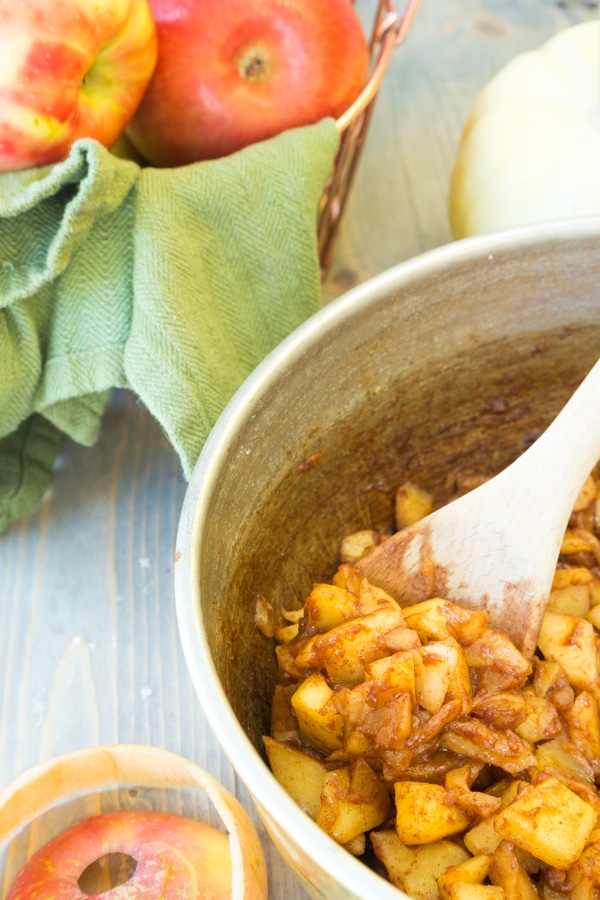 A copper pan filled with apple spice filling for turnovers with a wood spoon stirring the apples and a green napkin in the background