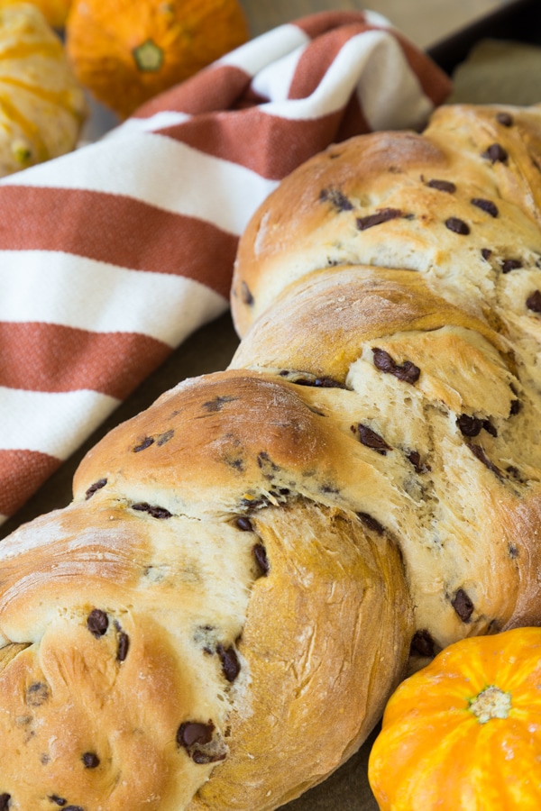 Pumpkin Vanilla Chocolate Chip Swirl bread baked on a board with a orange striped napkin and gourds