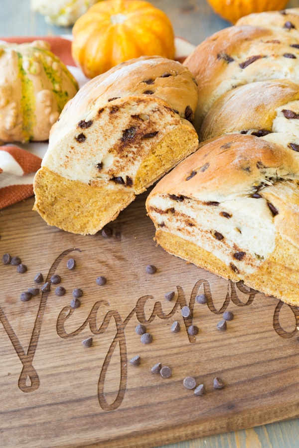 pumpkin vanilla chocolate chip bread on a wood board with an orange napkin and pumpkins in the background