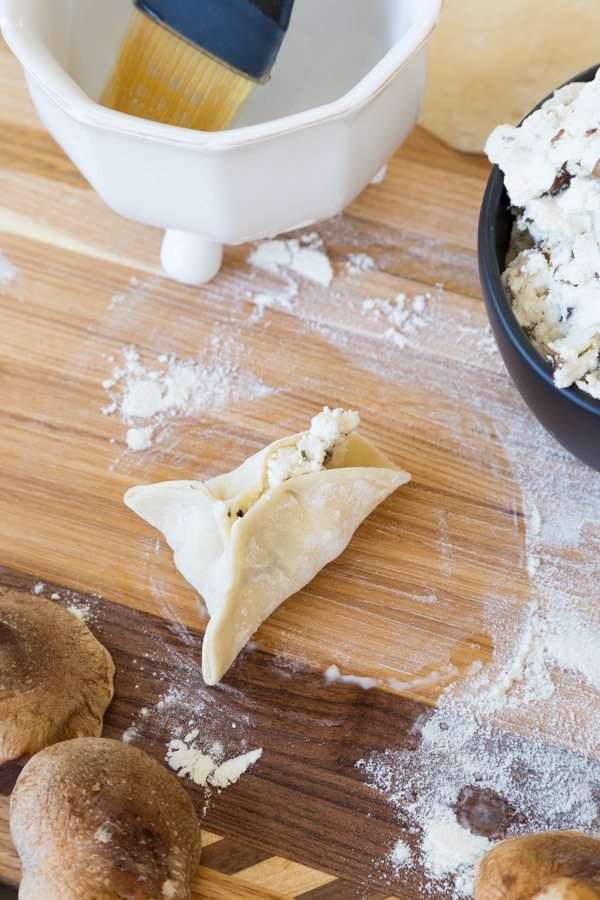 Stuffed wonton being folded on a wood board