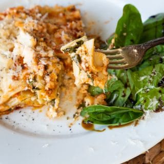 A slice of vegan spinach lasagna on a white plate with a side salad.