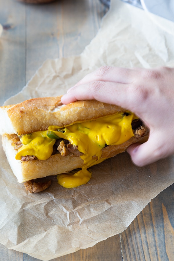 Philly Cheesesteak being held on a piece of unbleached parchment paper with cheese sauce running off the side