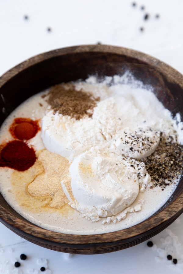 A wood bowl with milk, flour, and spices on a white table.