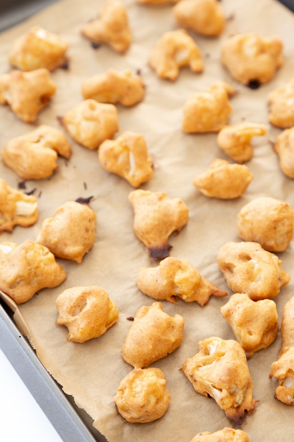Baked cauliflower poppers on a parchment lined baking sheet.