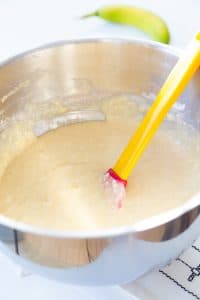 process shot of cake batter in a silver mixing bowl with a spatula in the bowl