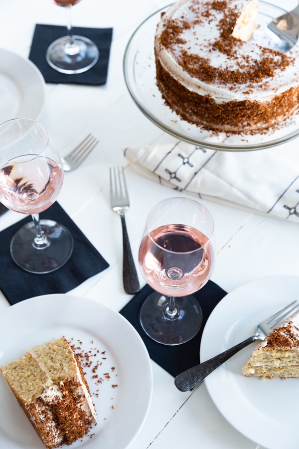 A white table with glasses of rose and a cake and white plates with slices of cake.