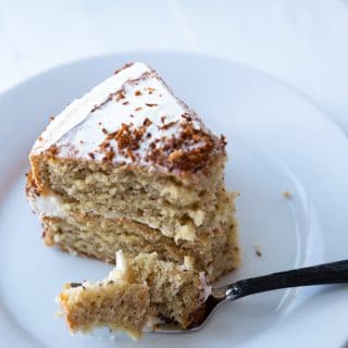 A slice of cake on a white plate with a fork and a piece of cake resting on it.