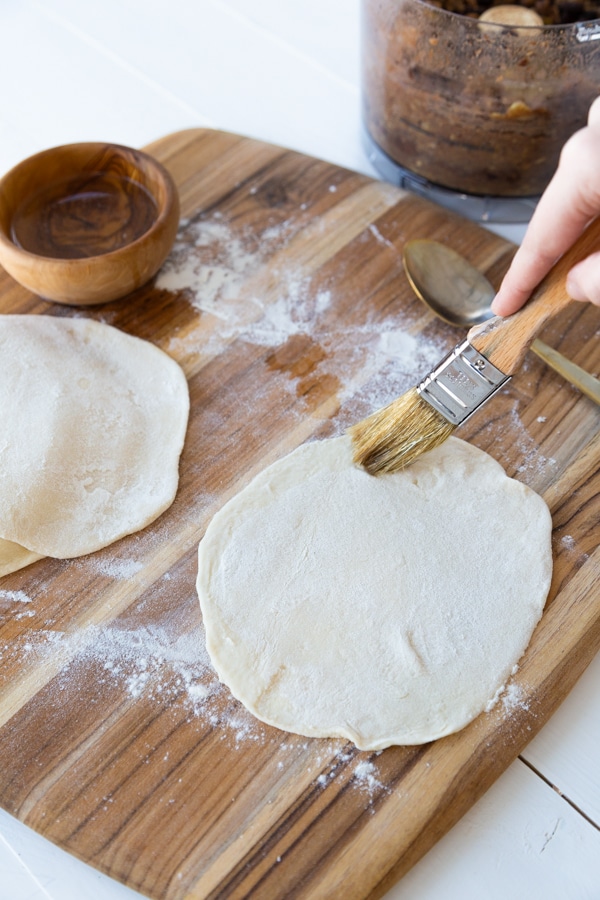 Two rounds of pasta dough being brushed with oil for empanadas