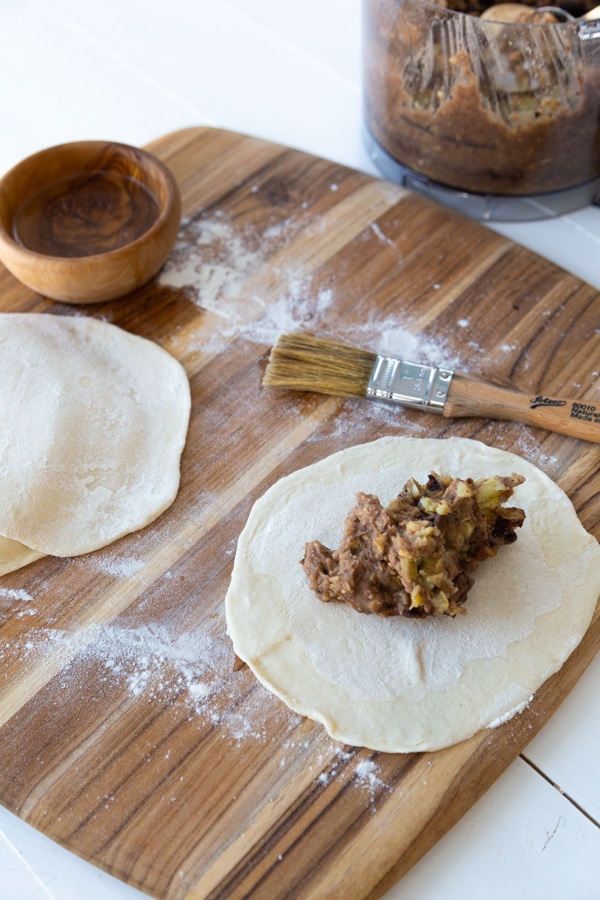 round empanada dough being filed with sweet potato and beans