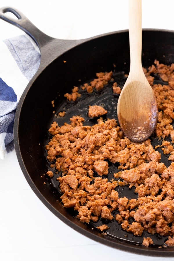 Cooking ground sausage in an iron skillet with a wood spoon