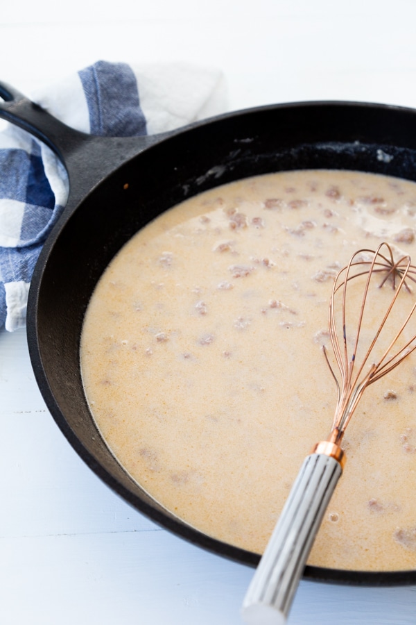 A copper whisk in an iron skillet with sausage gravy