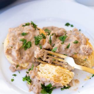 Biscuits and gravy on a white plate with a gold fork