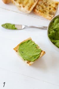 caprese avocado spread on bread with white board in the background and bowl of avocado spread in the background