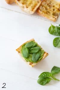 caprese sandwich with avocado spread and basil leaves on top of the avocado spread on a white wood board