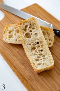 bread cut in half on a wood cutting board with serrated knife