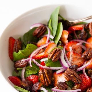 A white bowl with strawberry spinach salad and candied pecans
