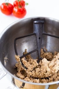 Pie dough in a silver mixing bowl with a paddle attachment.