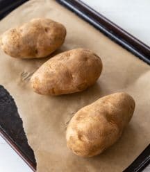 Three potatoes on a parchment lined baking sheet.