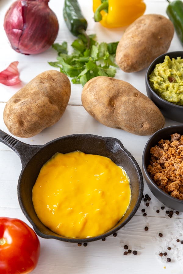 Cheese sauce in an iron skillet with potatoes, onion, tomato, and other ingredients for stuffed potatoes