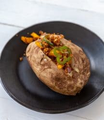 A baked potato on a black plate with a meaty filling stuffed in the center.