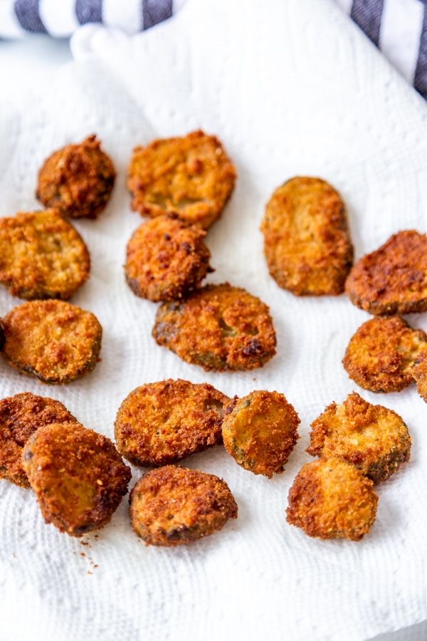 Fried pickles scattered on a paper towel next to a blue and white striped towel.