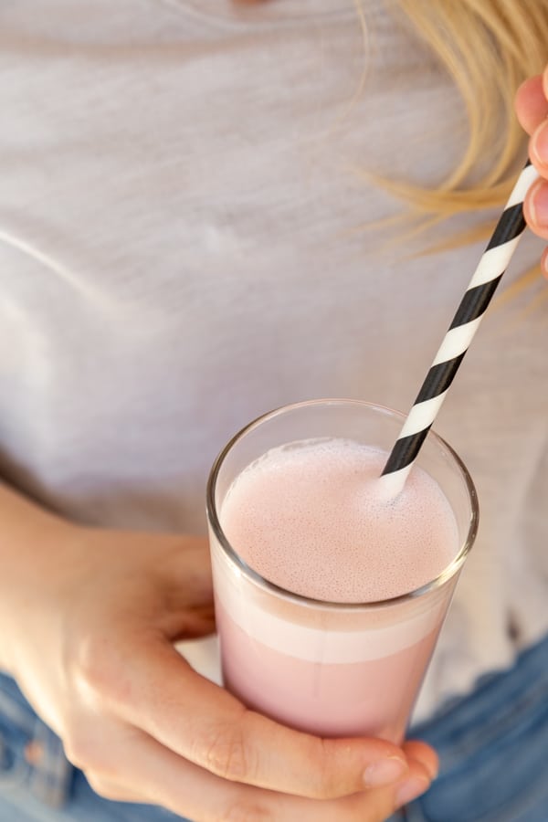 Hands holding a glass of strawberry milk with a black and white straw in the glass.