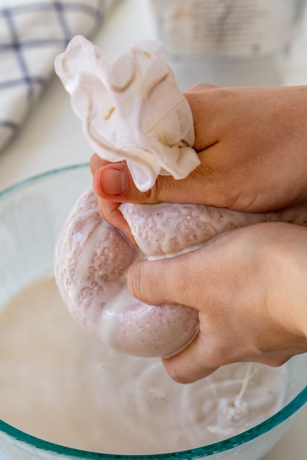 Two hands squeezing the liquid out of a nut bag filled with ground almonds over a glass bowl.