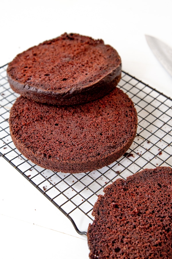 A chocolate cake sliced in half and the top sliced off on a wire rack.
