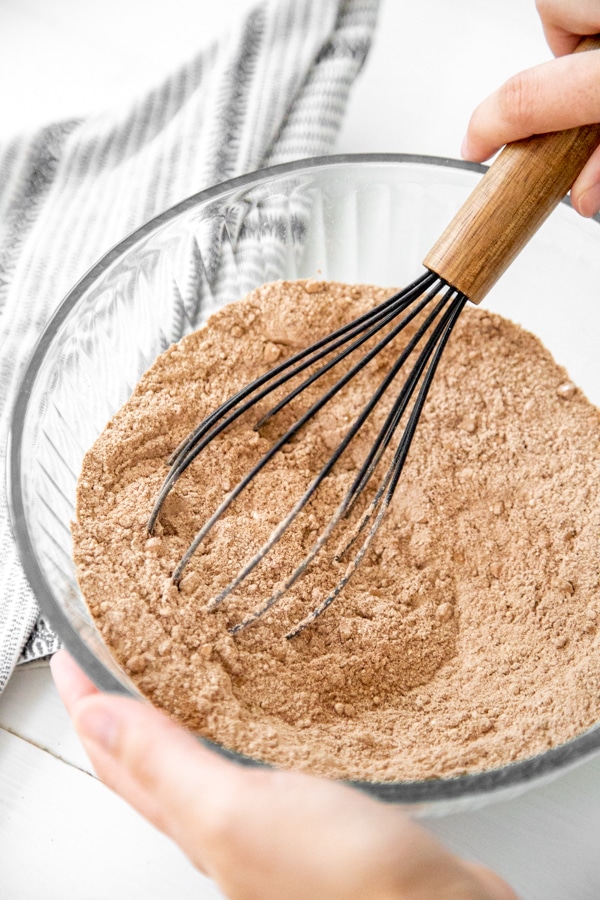 A hand whisking dry ingredients for a chocolate cake.