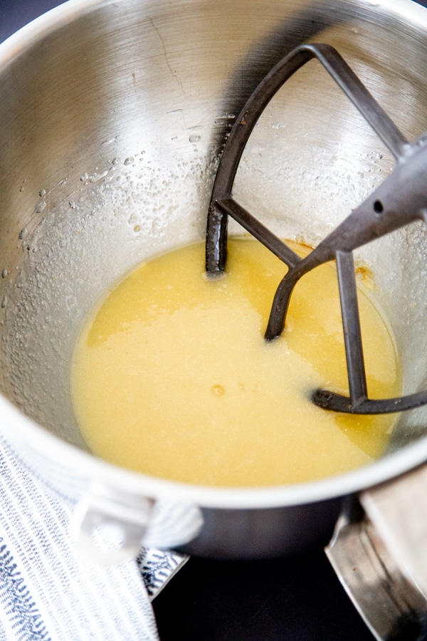 Sugar and eggs in a silver mixing bowl with a paddle mixer in the bowl.