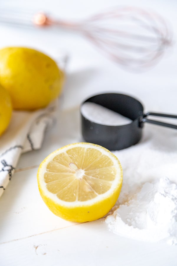 Lemons, flour, and sugar in a black measuring cup on a white wood board.