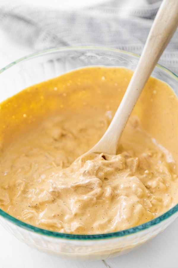 A wood spoon mixing shredded jackfruit and cheese sauce.