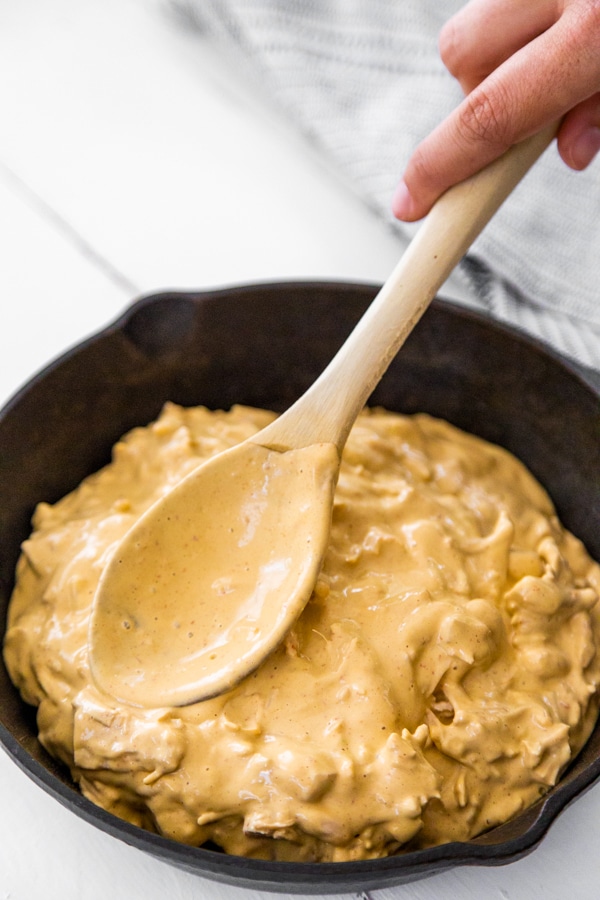 A spoon spreading buffalo chicken dip evenly in a cast iron pan.