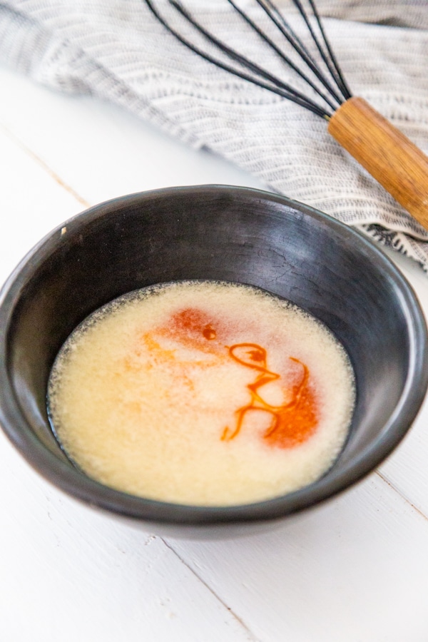 Melted butter and hot sauce in a black bowl with a whisk next to the bowl.