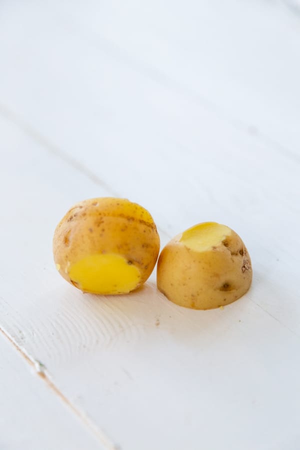 A potato cut in half and the ends trimmed off on a white wood table.