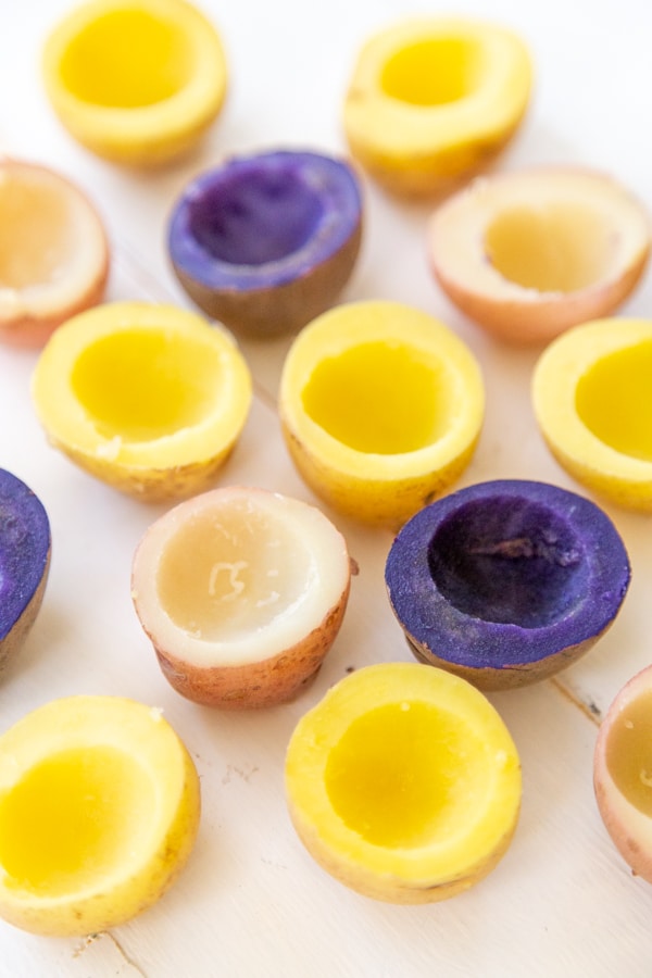 Tri-colored potatoes cut in half with the centers scooped out on a white table.