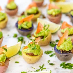 Potato taco bites on a marble board with a lime wedge and a glass of beer in the background.
