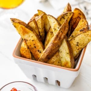 Home fries in a white dish with a small dish of ketchup and a glass of beer next to it.