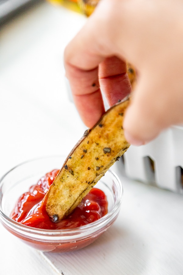 A hand dipping a French fry in ketchup.