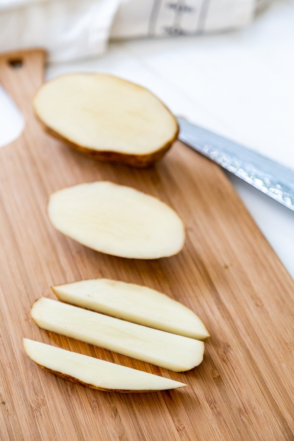 Sliced potatoes on a wood cutting board.