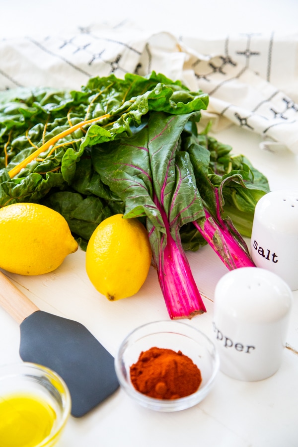 Rainbow Swiss chard, lemons, and spices on a white wood board.