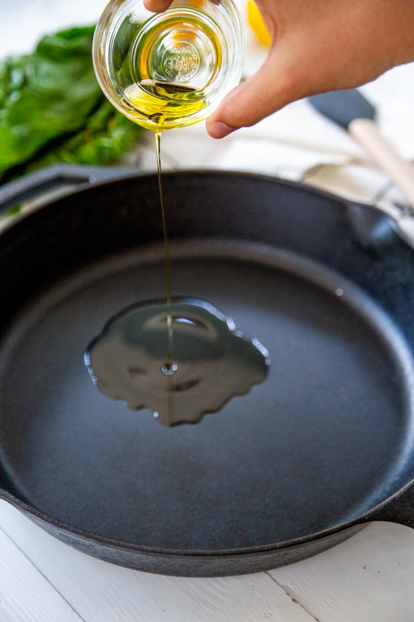 A hand pouring oil into a black iron skillet.