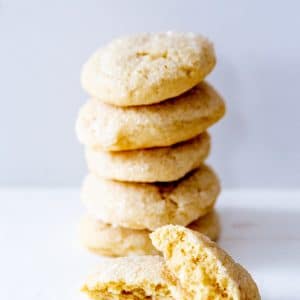 A stack of sugar cookies with on cut in half leaning on the stack.