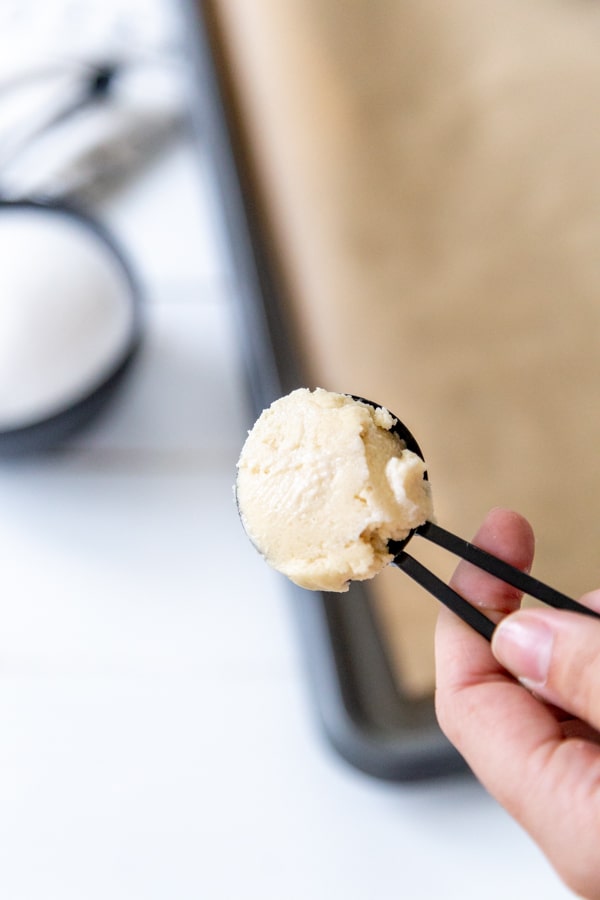 A black tablespoon with cookie dough being held over a baking sheet.
