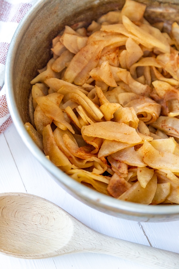 Chunky applesauce in a copper pan with a wooden spoon next to it.