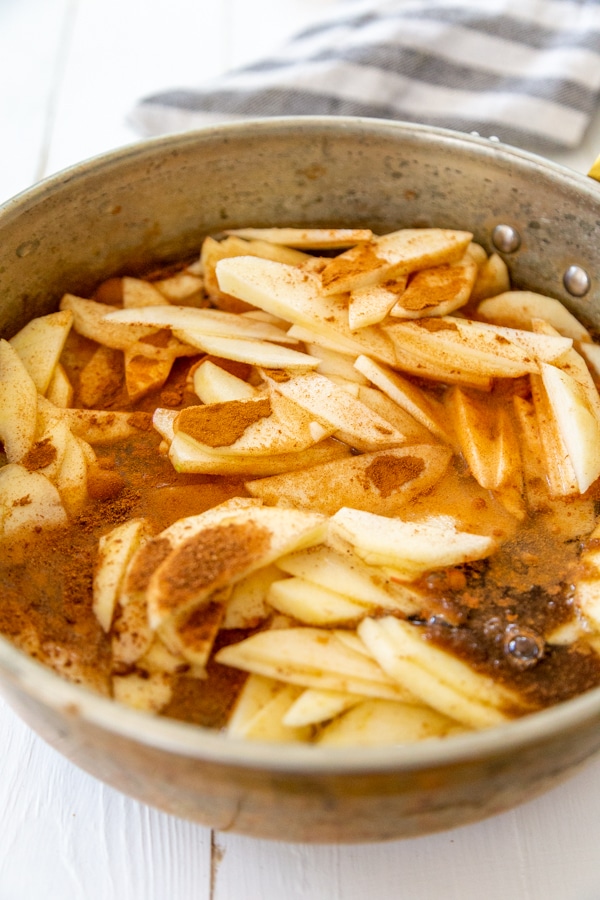 A copper pan with sliced apples and cinnamon sprinkled over the top of the apples.