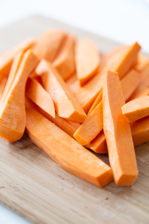 Sweet potatoes cut into fries on a wood cutting board.