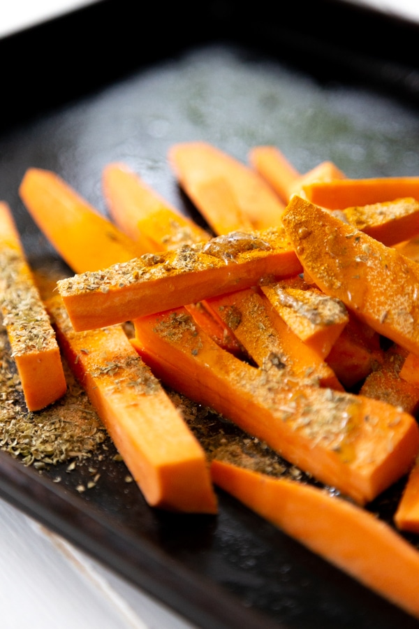 Raw sweet potato fries on a baking sheet with spices sprinkled on top.