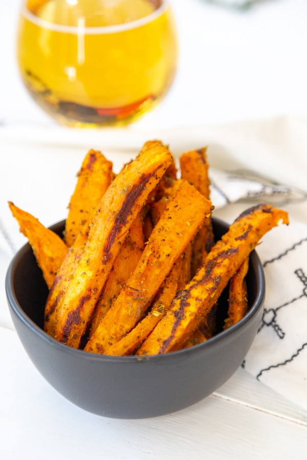 A black bowl filled with sweet potato fries and a glass of beer behind it.